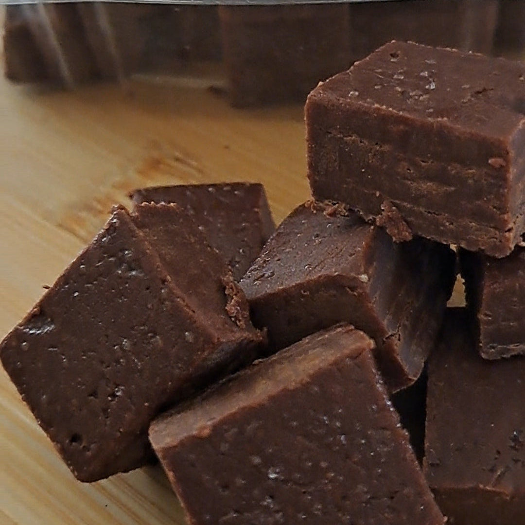 Chocolate fudge pieces on a wooden surface with a clear plastic container in the background.